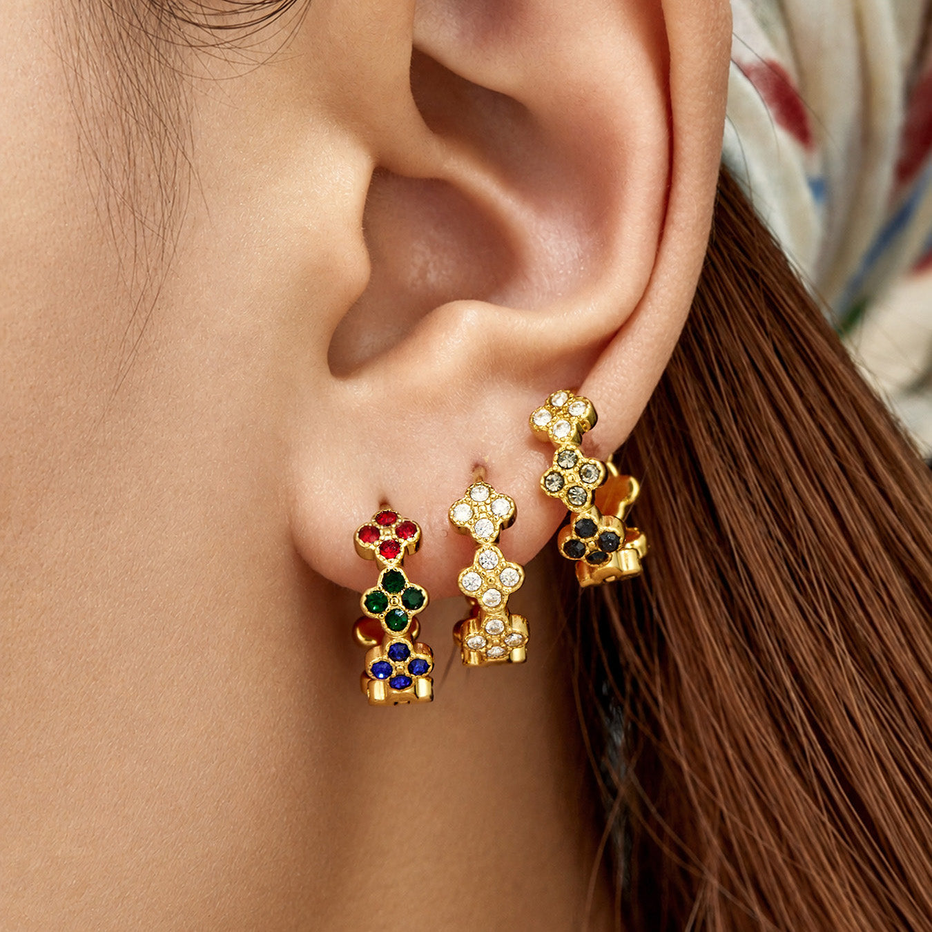 Model wearing gold four-leaf clover huggie earrings with multicolor cubic zirconia