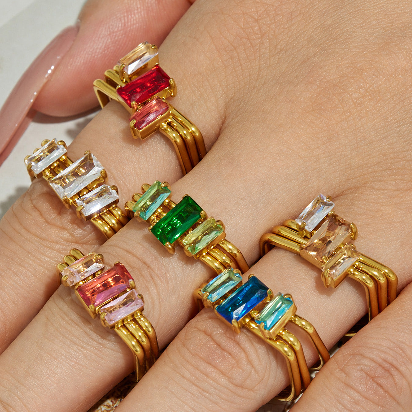 Multiple colorful CZ statement rings in white pink green and blue styled on a model hand