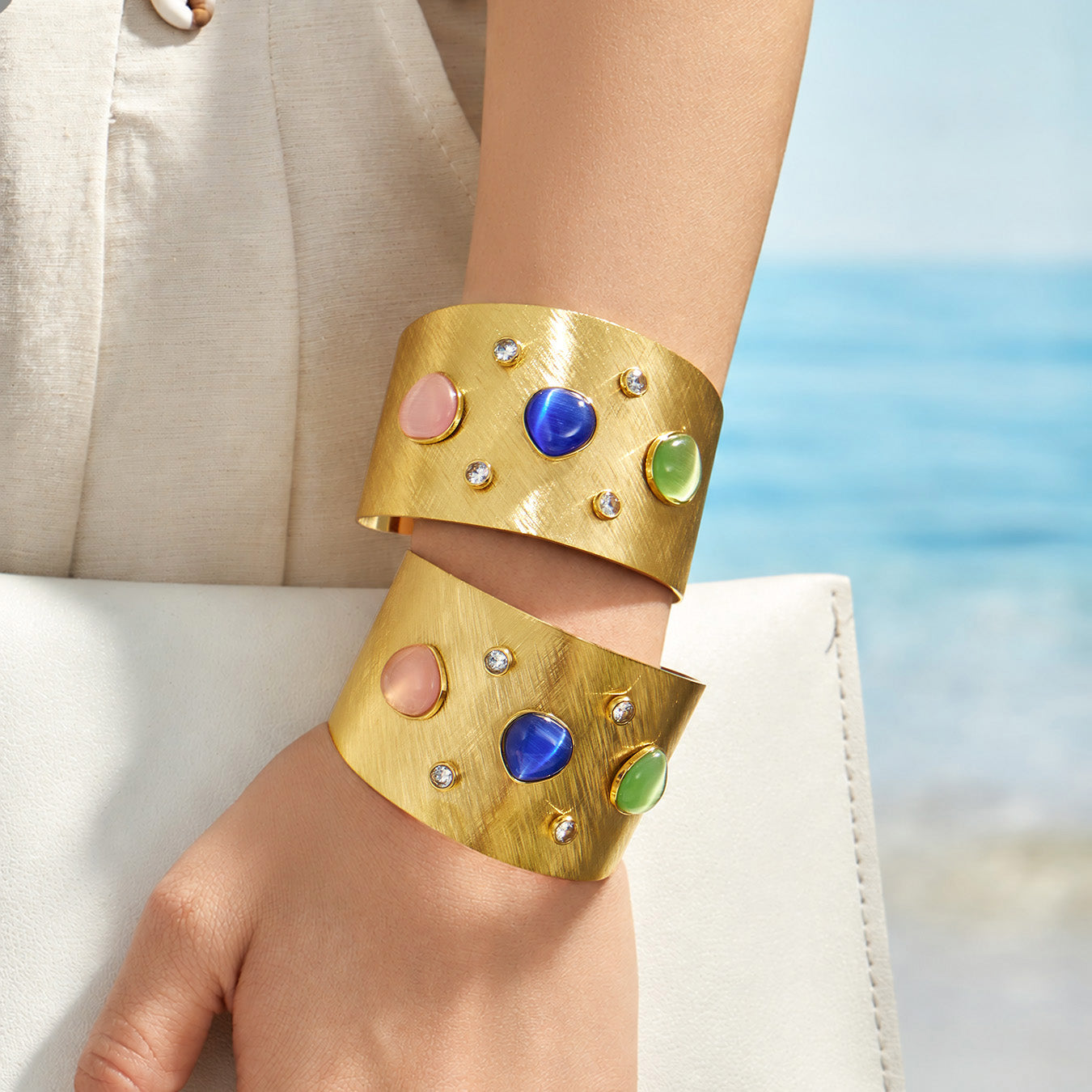 Two multicolor wide cuff bracelets styled on a model wrist near the beach