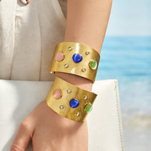 Two multicolor wide cuff bracelets styled on a model wrist near the beach