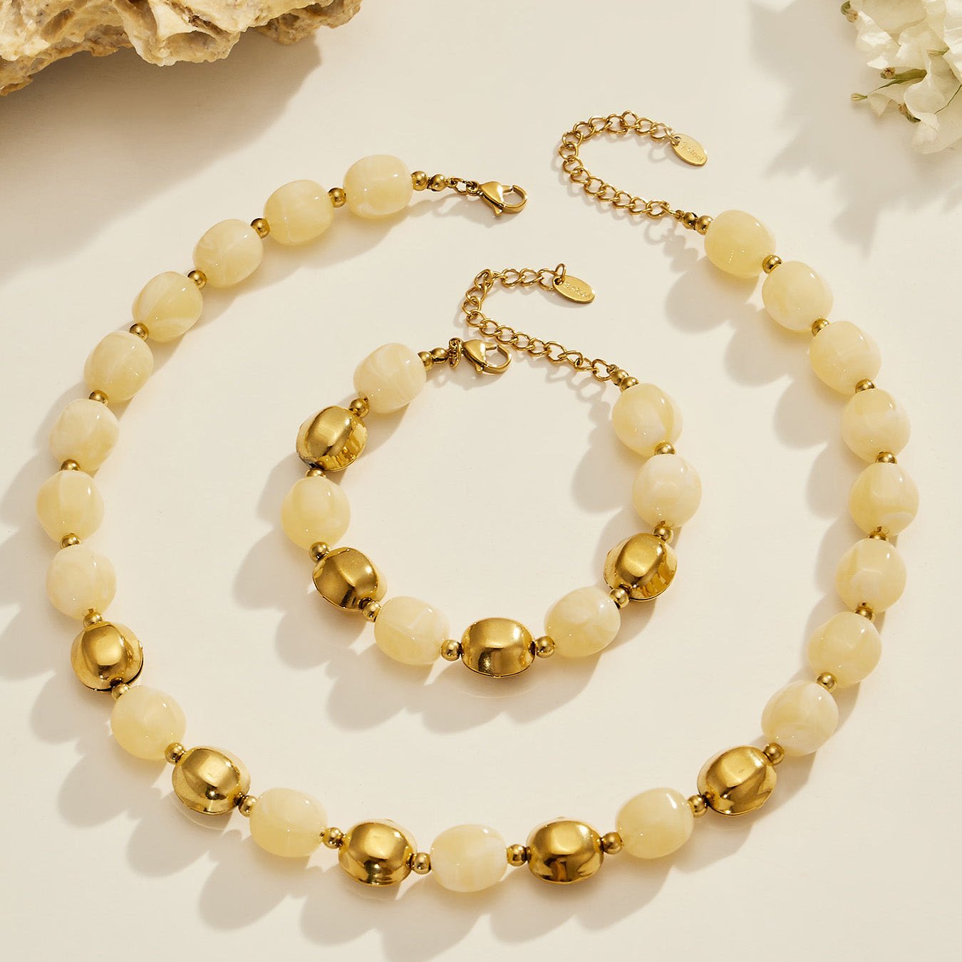 Flat lay of a light neutral resin bead necklace and bracelet set with stainless steel accent beads.