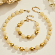 Flat lay of a light neutral resin bead necklace and bracelet set with stainless steel accent beads.