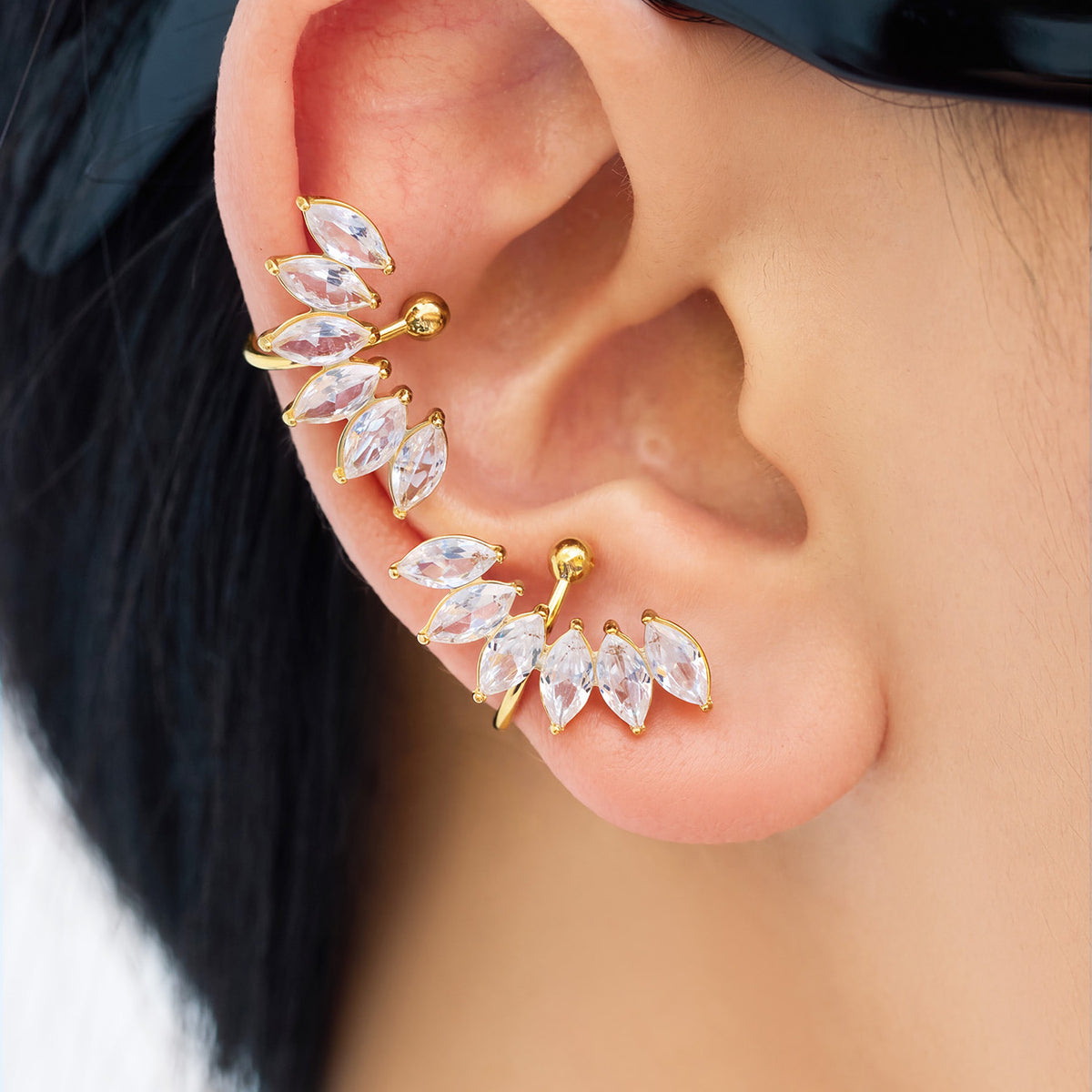 Close-up of a gold-tone curved leaf ear cuff worn along the ear with clear marquise-shaped stone accents