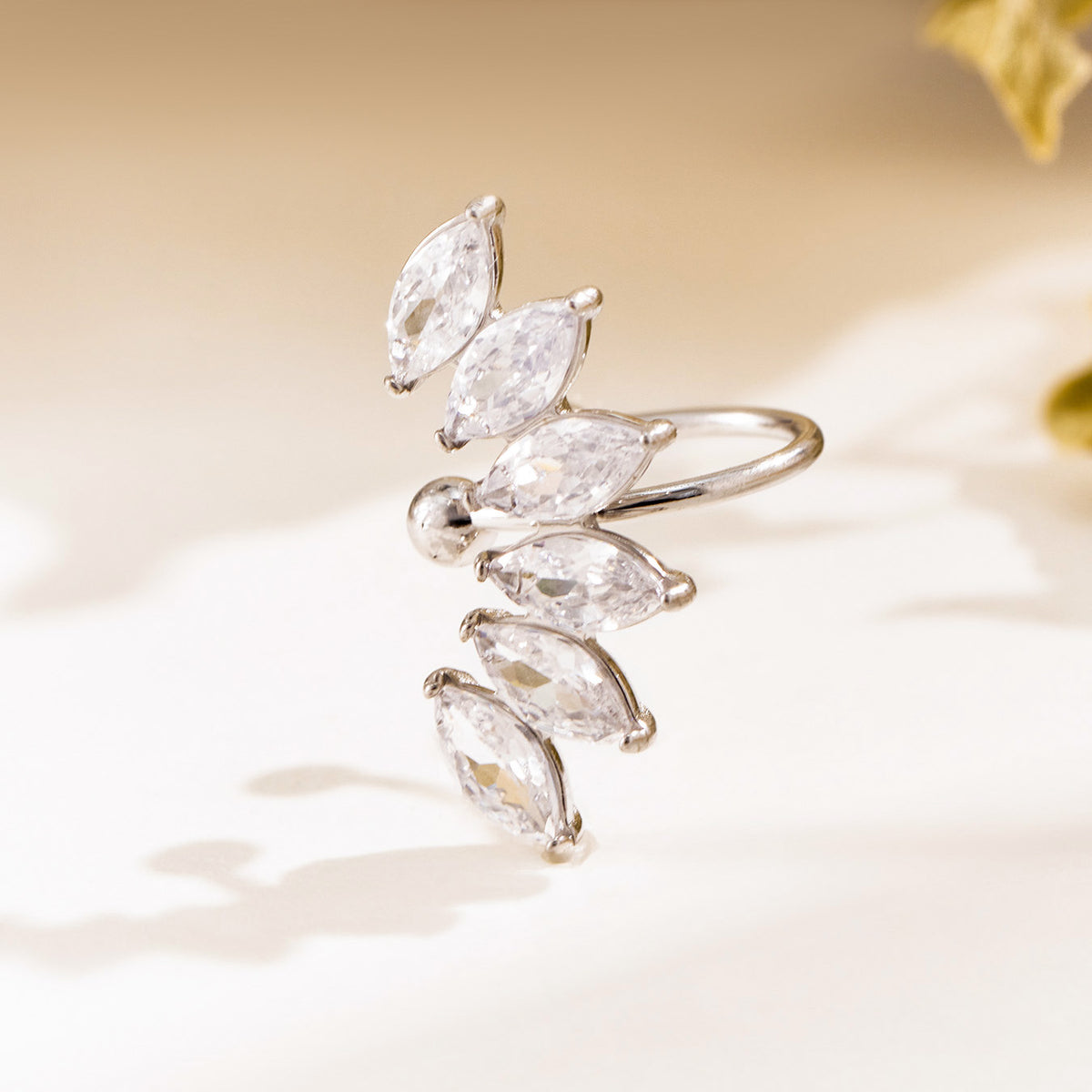 Silver-tone leaf ear cuff displayed on a neutral background with clear marquise-shaped stones and polished metal bands