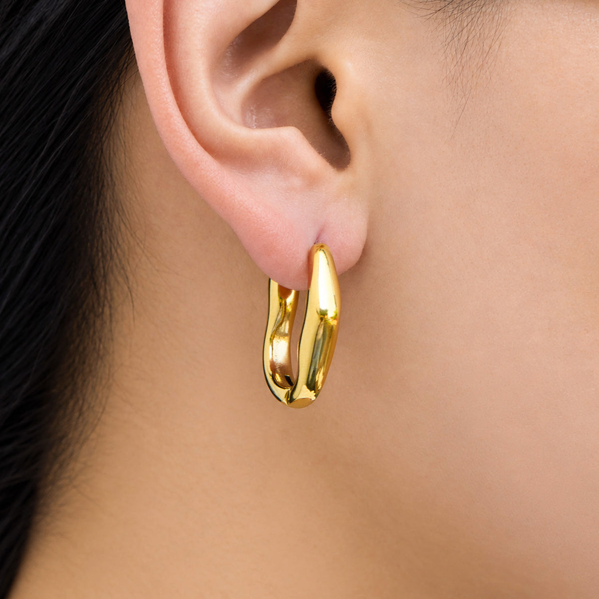 Model wearing a polished gold irregular hoop earring with a thick sculptural silhouette and rounded wavy edges