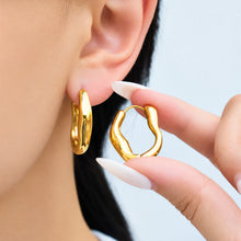 Model holding a gold irregular hoop earring beside her ear to demonstrate its curved shape and size