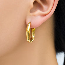 Close-up of a model wearing a gold sculptural hoop earring with a fluid asymmetrical outline and polished metal surface
