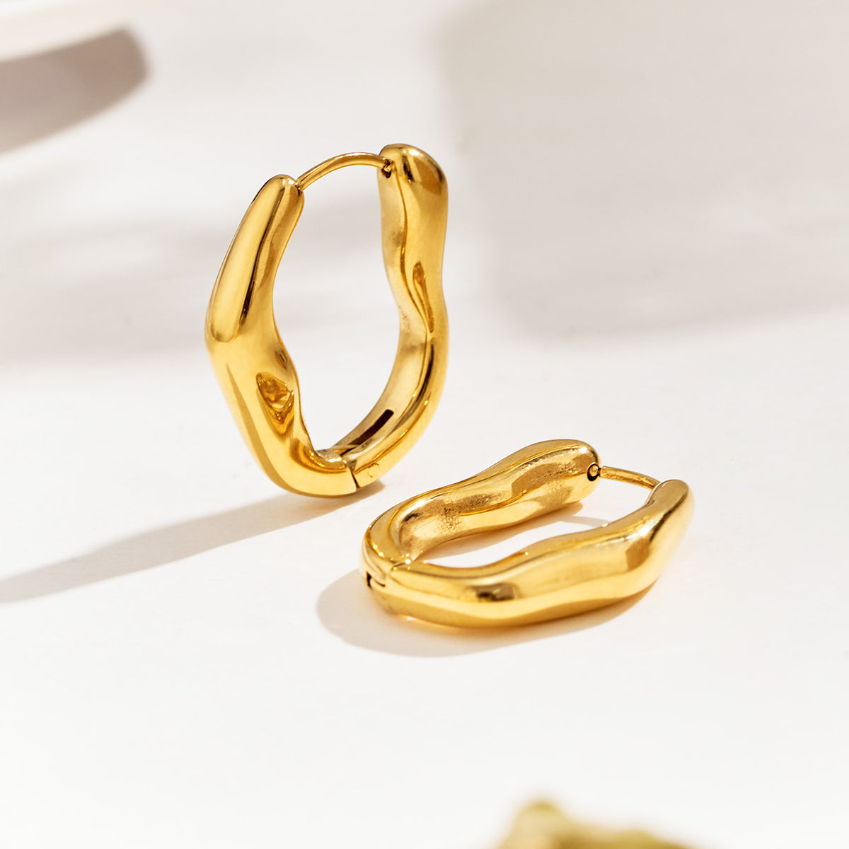 Two gold-tone organic hoop earrings displayed at different angles, highlighting their thick curved profiles and hinged construction