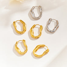 Gold and silver sculptural hoop earrings arranged on a light surface, showing contrasting polished finishes and wavy shapes