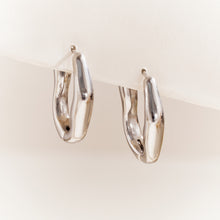 Pair of silver-tone irregular hoop earrings displayed on a neutral background with smooth asymmetric curves