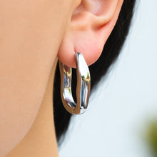 Model wearing a silver-tone stainless steel organic hoop earring with a polished finish and flowing irregular curves
