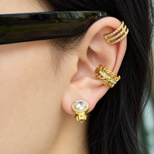 Model wearing a gold round halo clip-on earring on the earlobe, styled with layered gold ear jewelry