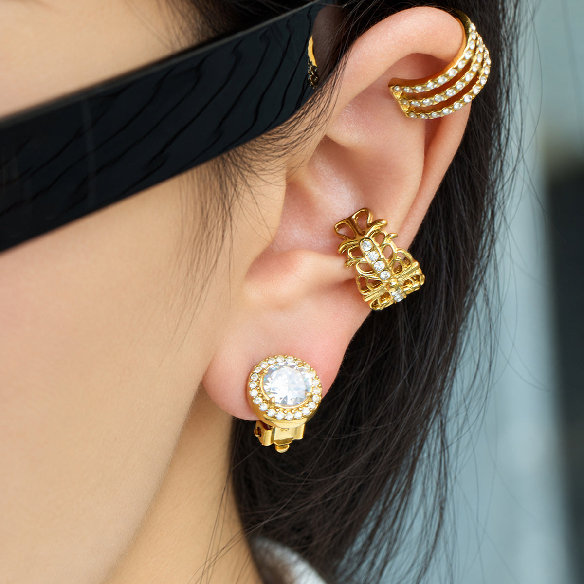 Close-up of a gold halo clip-on earring worn with multiple gold ear cuffs, highlighting the round stone and pavé-style border