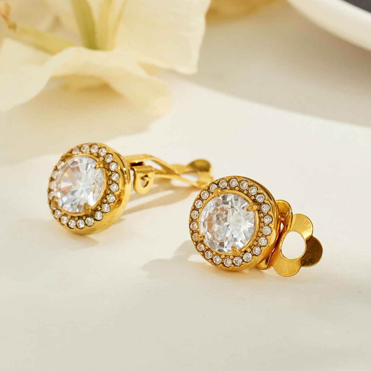 Pair of gold-tone halo clip-on earrings displayed on a neutral background, showing the faceted center stones and gold clip-on fittings