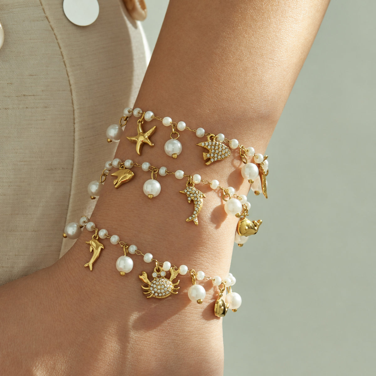 Gold stainless steel pearl charm bracelets with ocean motifs styled together on a model wrist