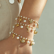 Gold stainless steel pearl charm bracelets with ocean motifs styled together on a model wrist
