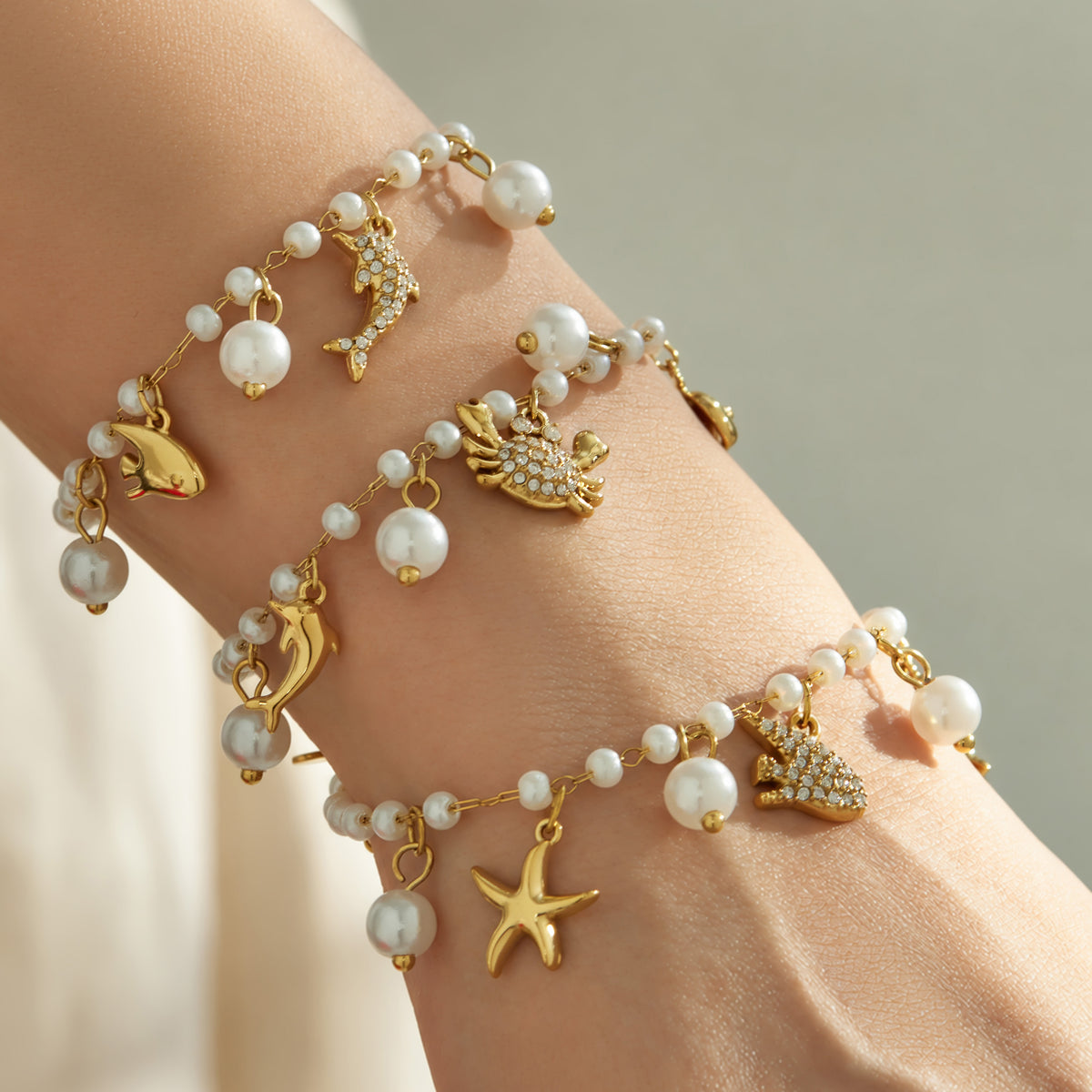 Layered gold marine charm pearl bracelets with starfish and ocean-inspired charms on a model wrist