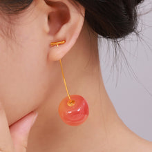 Orange-red cherry drop earrings with long gold-tone stems worn by a model