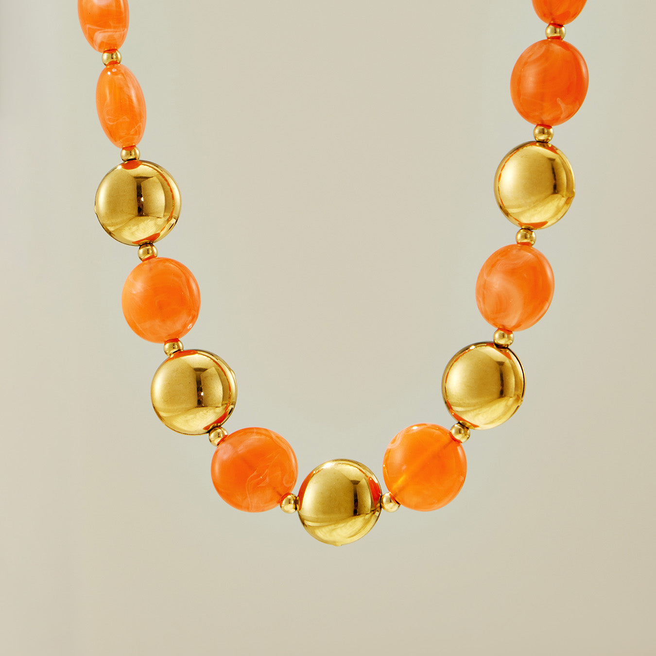 Flat lay close-up of an orange-toned resin bead necklace with gold-tone accents for boutique jewelry display.