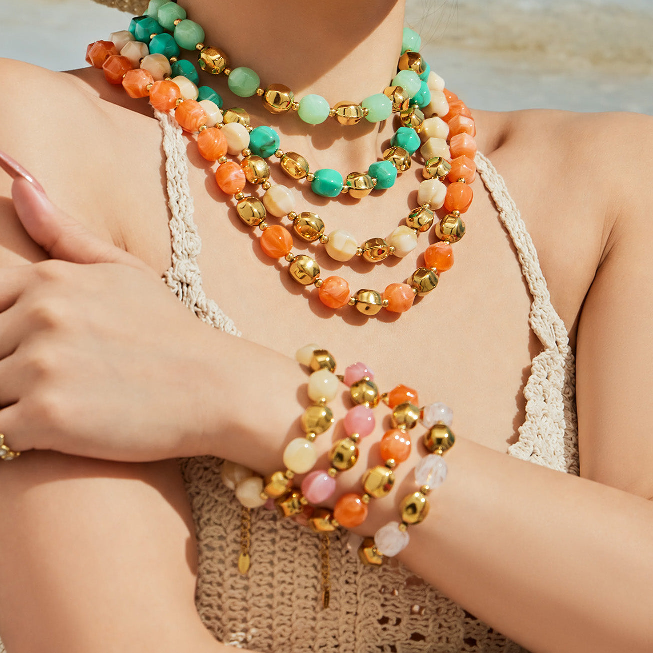 Model wearing an orange resin bead necklace with stacked matching bracelets in a colorful summer jewelry look.