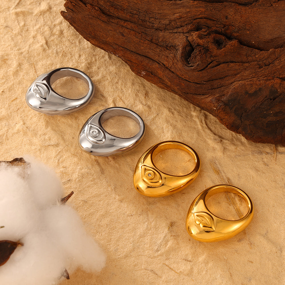 Gold-tone and steel-tone organic cutout rings displayed beside wood