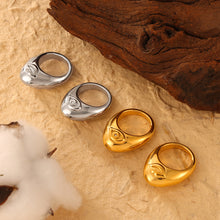 Gold-tone and steel-tone organic cutout rings displayed beside wood
