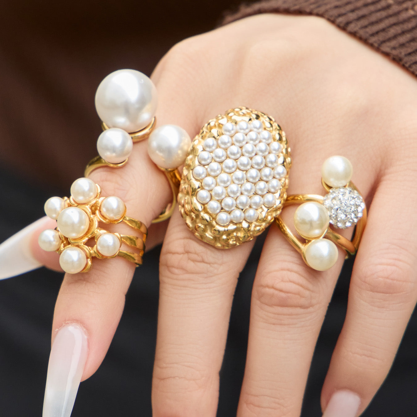 Close-up of an oval pearl cluster ring and sculptural open pearl rings worn together