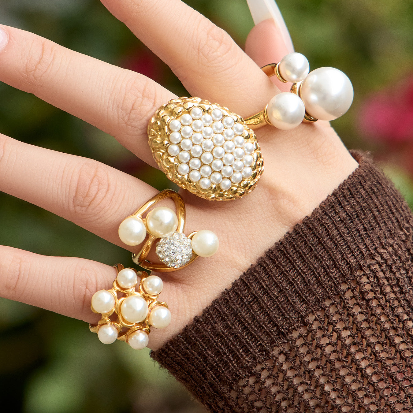 Oversized oval pearl cluster and sculptural pearl rings shown against a green background