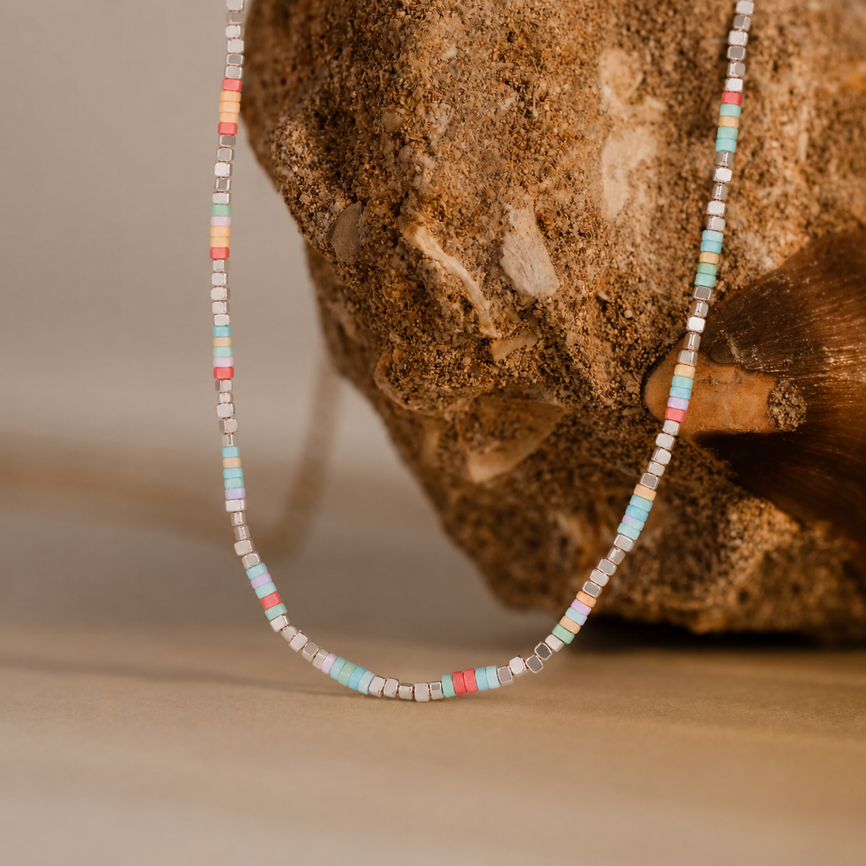 Natural stone heishi bead necklace with pastel colorful beads styled on stone background for resort jewelry collections