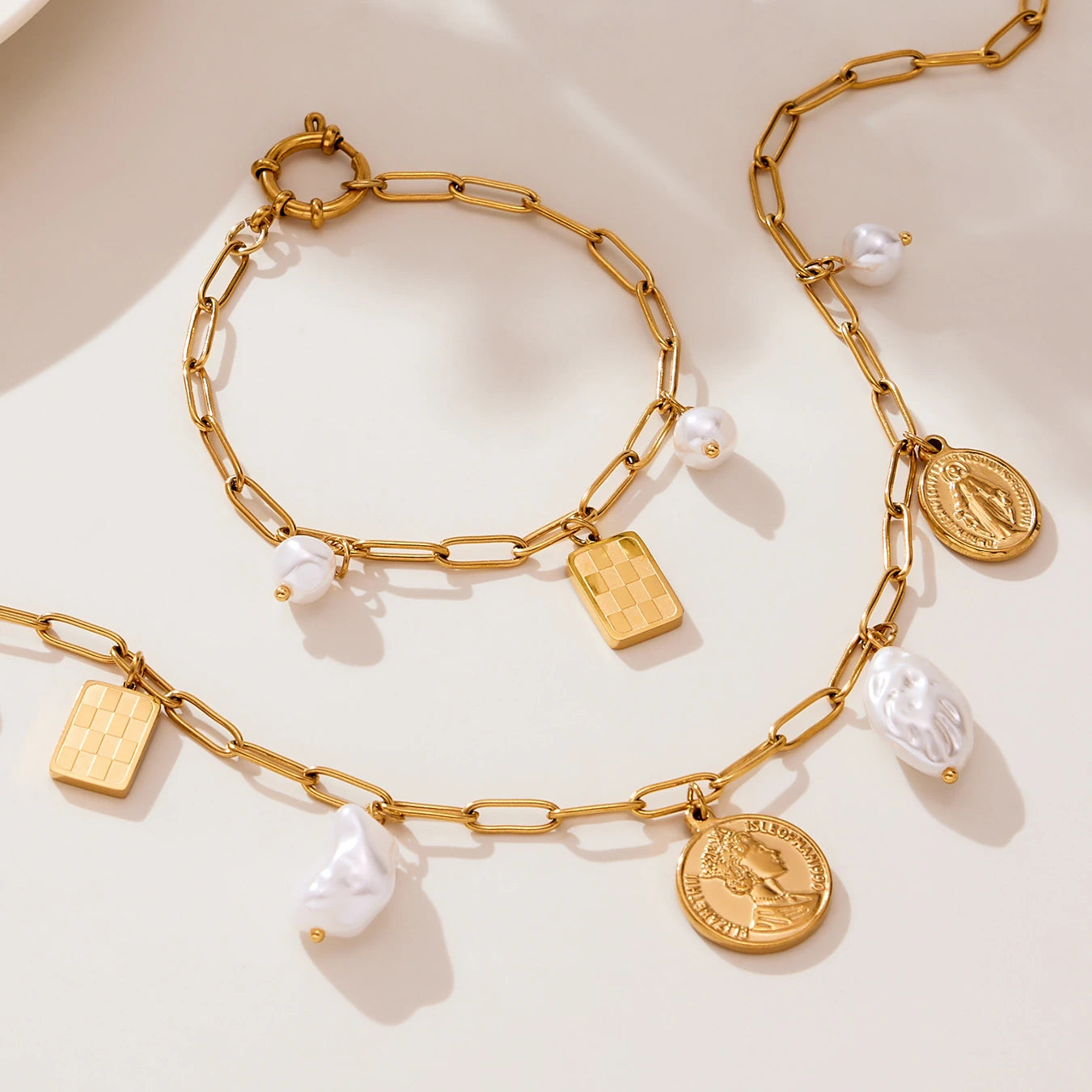 Gold paperclip charm necklace and bracelet flat lay with coin and pearl-look pendants