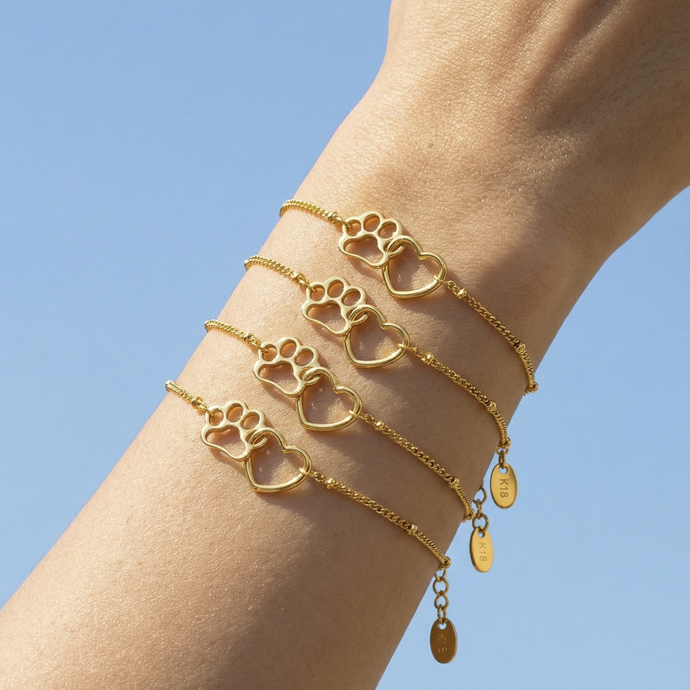 Gold paw heart chain bracelet styled with layered bracelets on the wrist