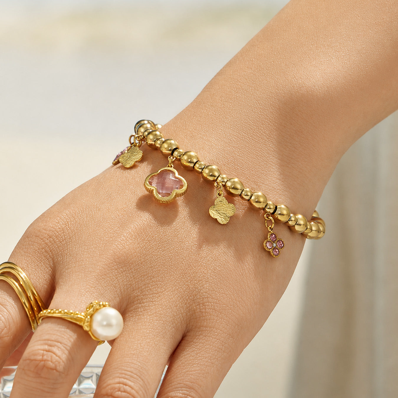 Pink clover beaded charm bracelet worn on a model hand with gold rings