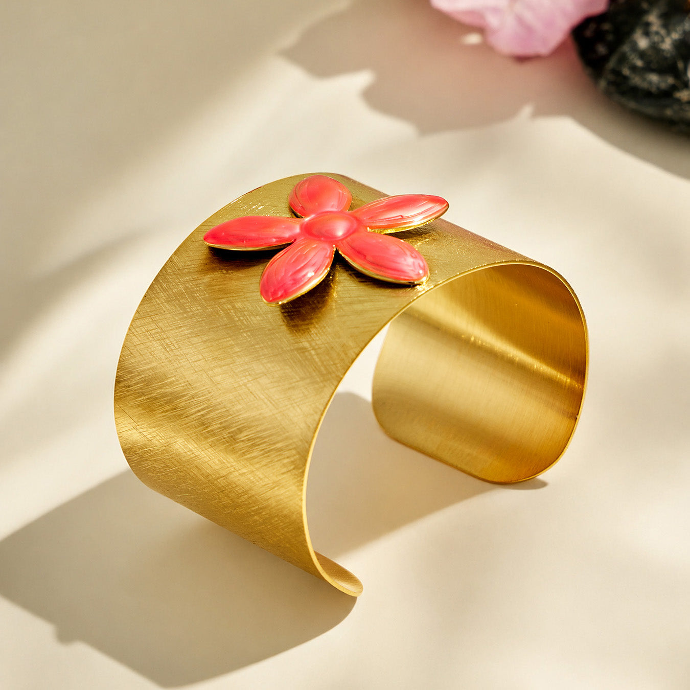 Angled product view of a gold cuff bracelet with a raised pink enamel flower