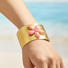 Pink enamel flower gold cuff bracelet worn on a model wrist by the sea