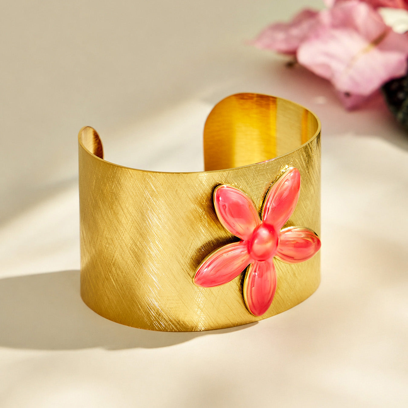 Front view of a wide brushed gold cuff bracelet with a pink enamel flower