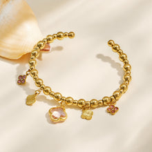 Pink four-leaf clover charm bracelet with a gold beaded chain displayed on fabric
