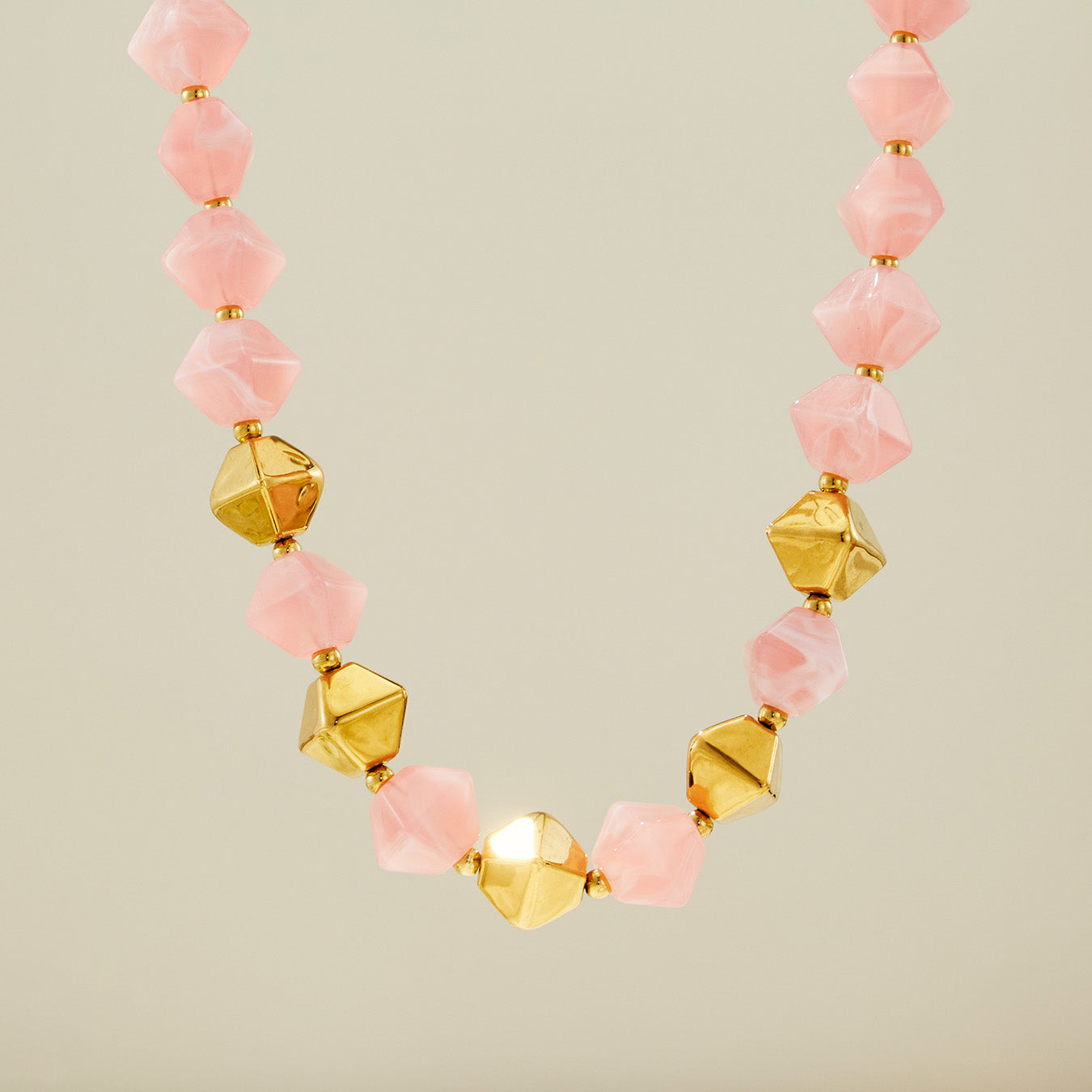 Pink faceted resin bead necklace with gold stainless steel accent beads displayed on a neutral background