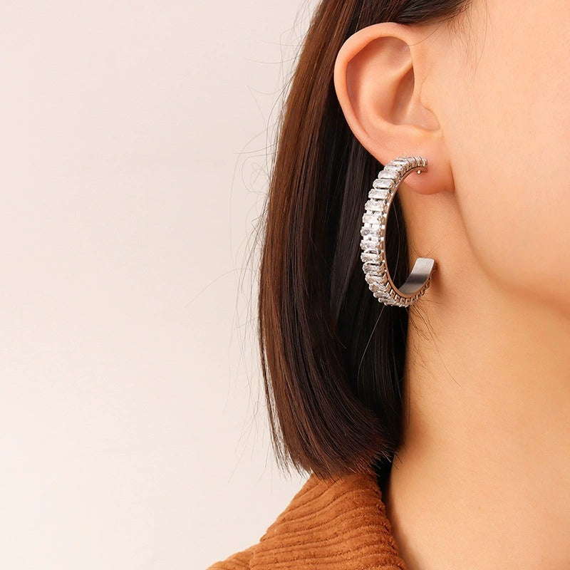 Model wearing polished steel C-shaped hoop earrings with clear cubic zirconia accents