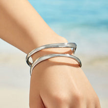 Polished steel double loop cuff bracelet worn on a model wrist near the sea