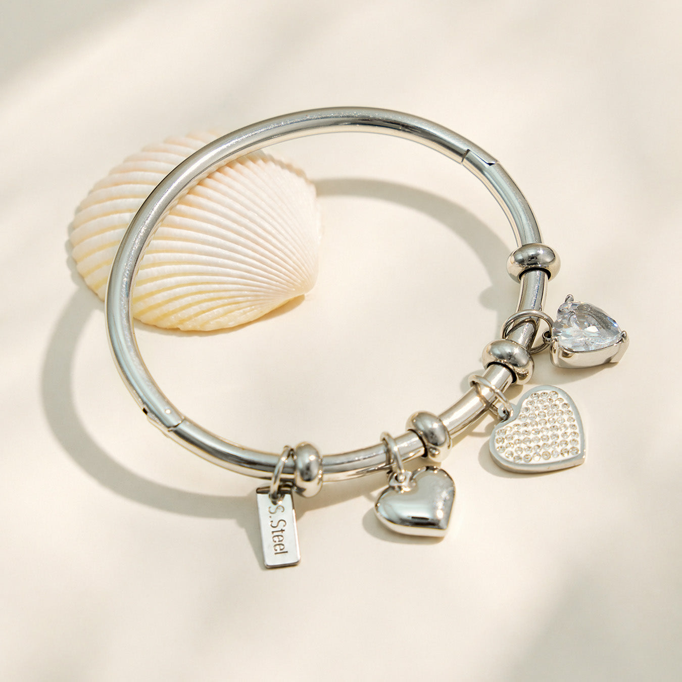 Polished steel heart charm bangle bracelet with clear zircon details in a flat lay