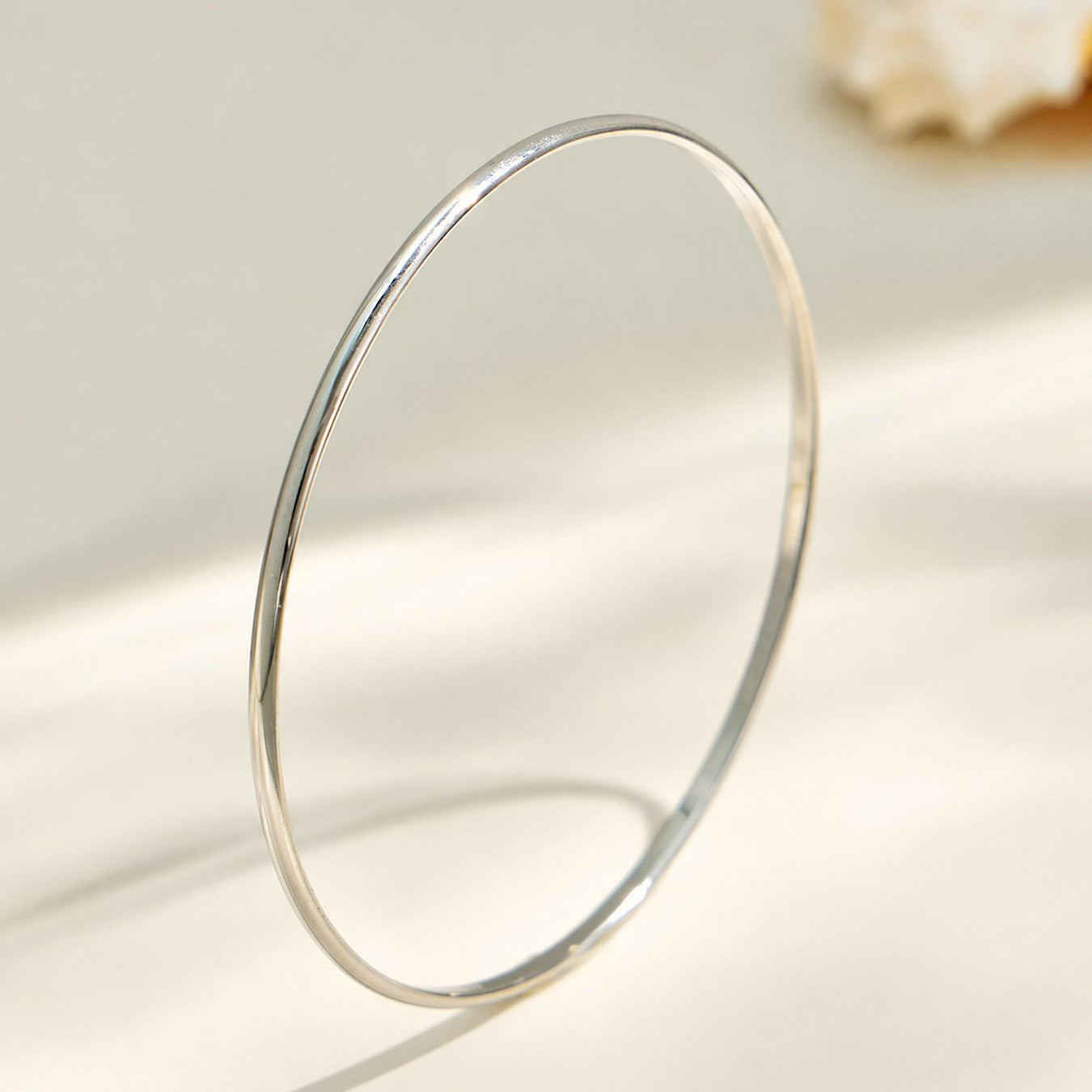 Polished steel slim stainless steel stackable bangle on a light background