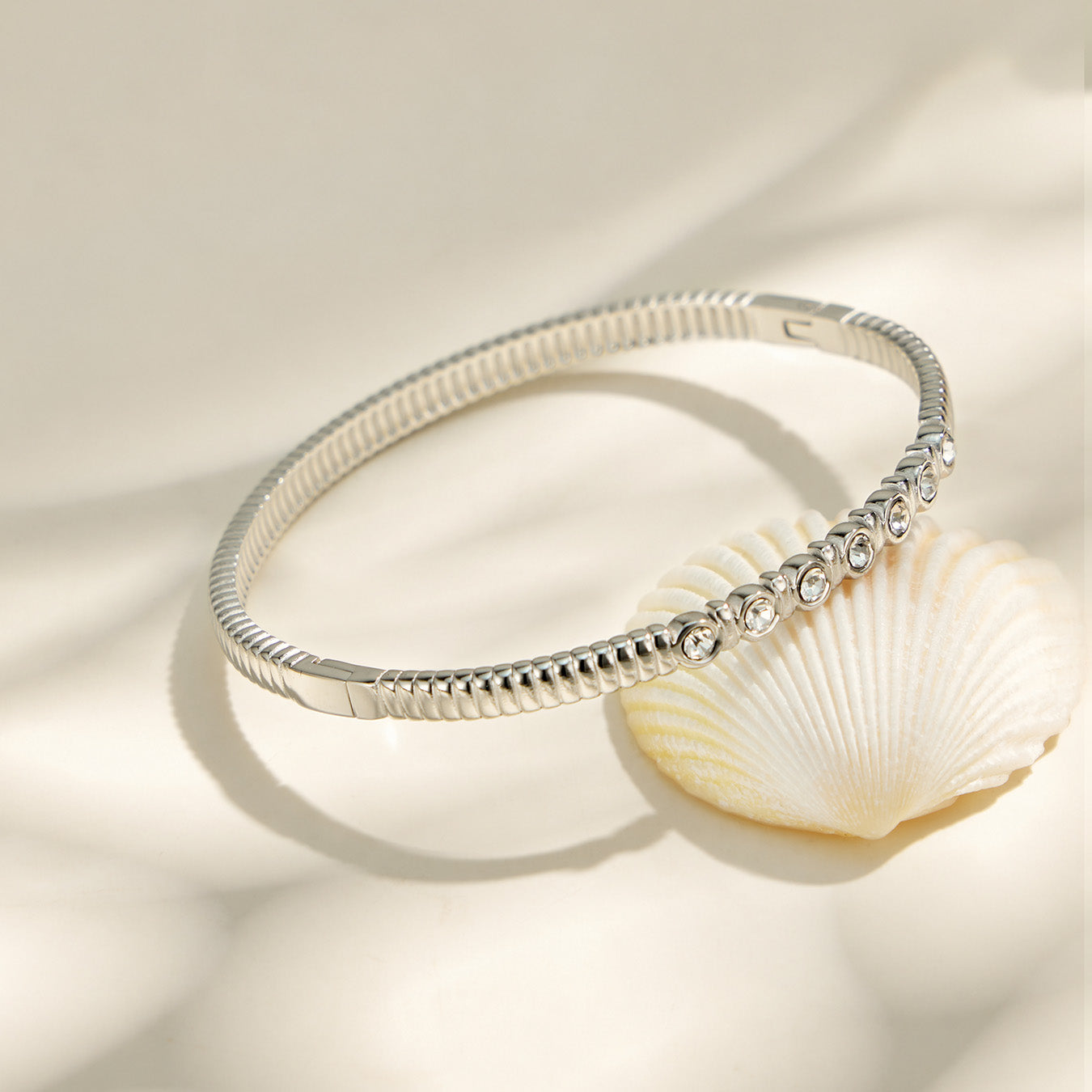 Polished steel zircon bangle displayed with gold bracelet details in a neutral flat lay
