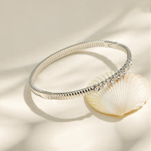 Polished steel zircon bangle displayed with gold bracelet details in a neutral flat lay