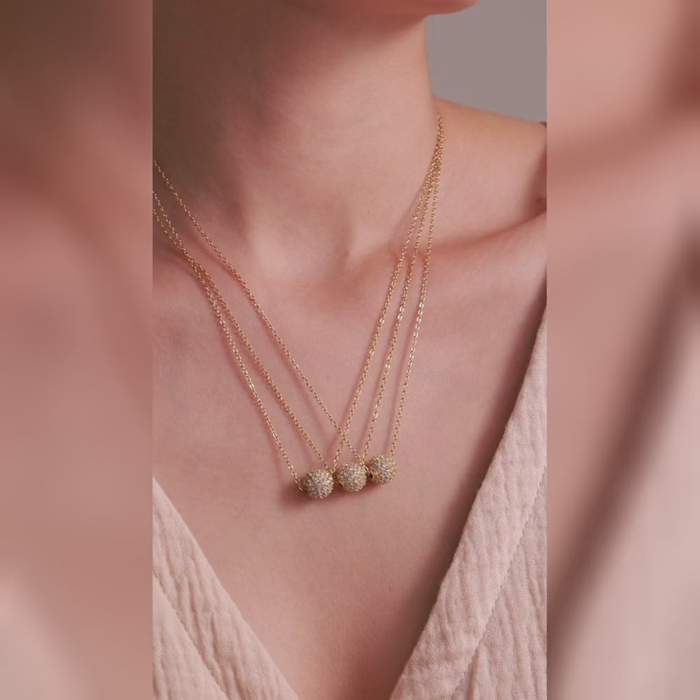 Three gold-tone chain necklaces with clear-stone pavé ball pendants, shown on a model.