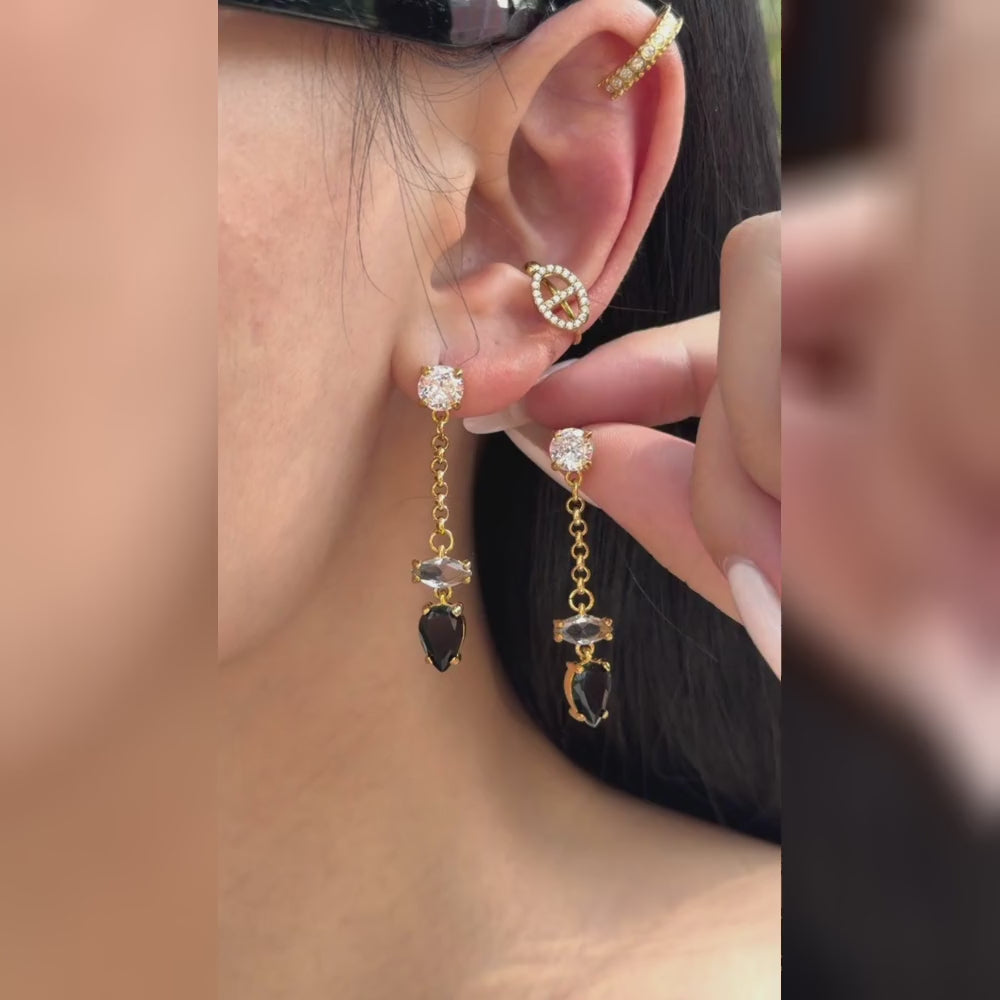 Gold-tone chain drop earrings with clear stone accents and black teardrop stones, shown on a model.