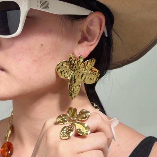 Model wearing oversized textured gold-tone statement earrings and a sculptural gold-tone ring.