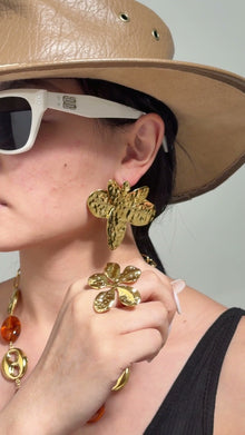 Model wearing oversized textured gold-tone statement earrings and a sculptural gold-tone ring.