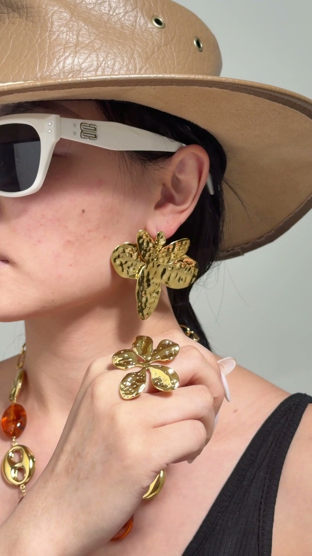 Model wearing oversized textured gold-tone statement earrings and a sculptural gold-tone ring.