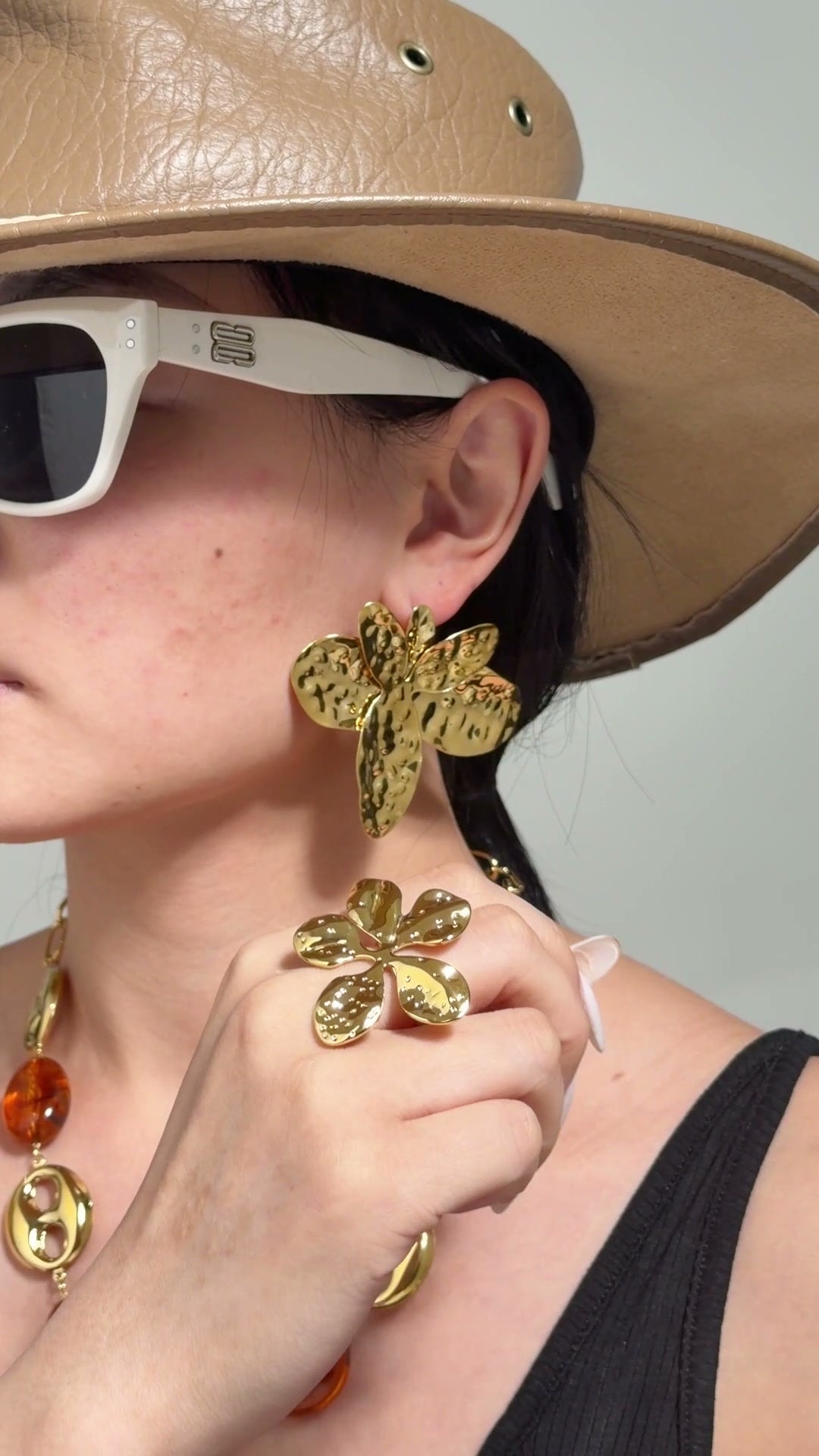 Model wearing oversized textured gold-tone statement earrings and a sculptural gold-tone ring.