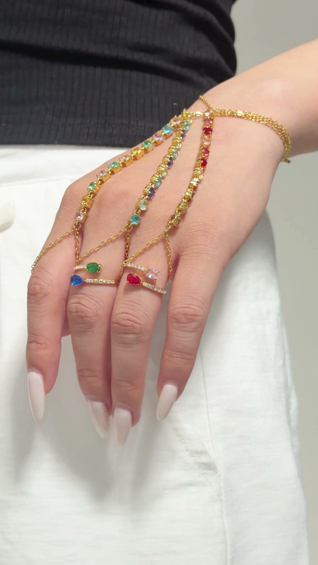 Gold-tone hand chains with multicolored stones draped from the wrist to the fingers.
